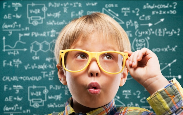 Cute little schoolgirl in glasses on blackboard