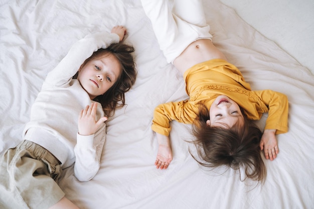 Милые младшие сестрички развлекаются на кровати дома, вид сверху