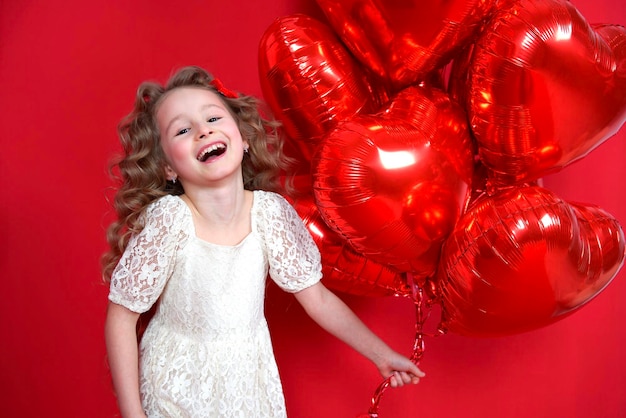 Cute little small child kid beautiful happy excited girl with red heart shaped balloons in dress