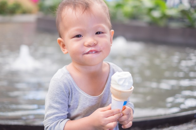 Cute little smiling Asian 1 year old toddler baby boy child eating soft serve ice cream