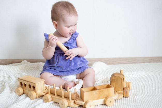 木製の電車で遊ぶかわいい笑顔の白人の女の赤ちゃん。小さな子供のためのおもちゃ。初期の開発