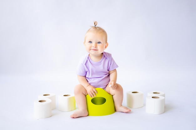 Una bambina sorridente carina è seduta su una pentola con rotoli di carta igienica isolati su sfondo bianco