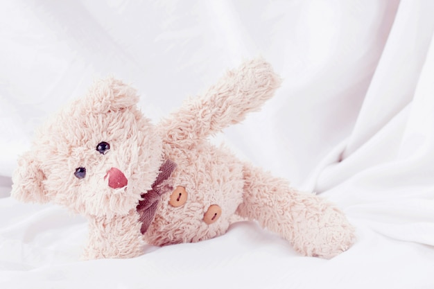 Cute little teddy bear lay down on the bed.