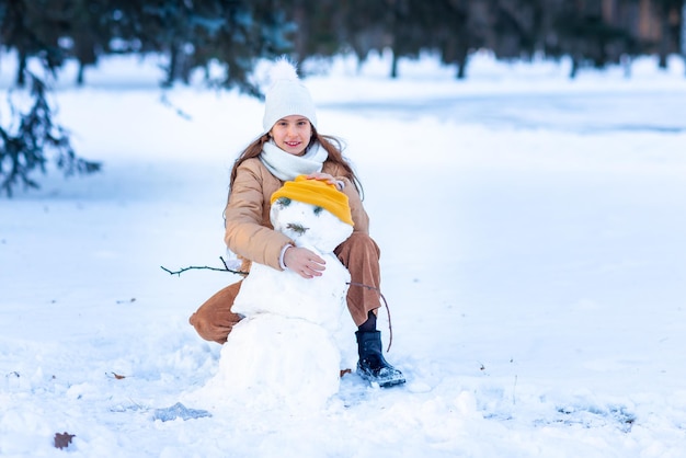 Cute little teenage girl having fun playing making snowman in the snowy winter forest