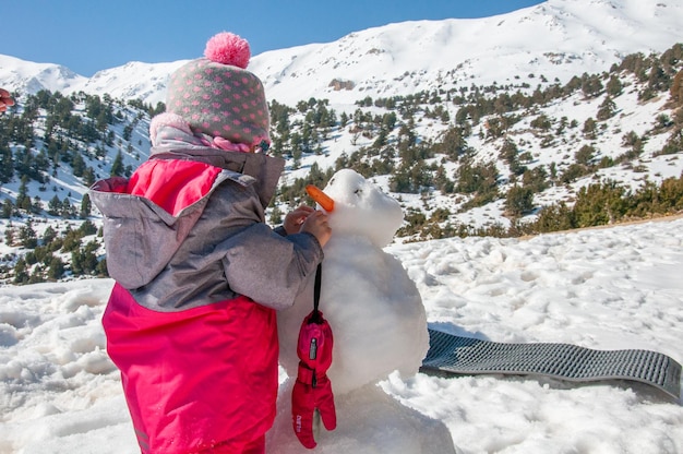 Cute little toddler girl making snowman on beautiful winter day