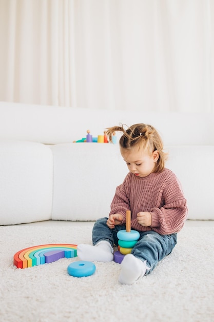 Фото Милая маленькая девочка, играющая дома с экологическими деревянными игрушками счастливый ребенок режет овощи и фрукты игрушечным ножом ребенок играет в развивающие игры