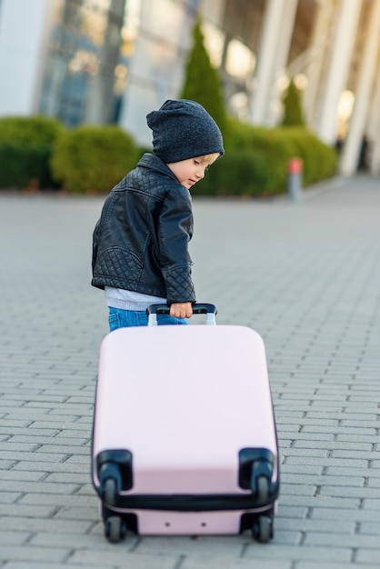 Cute little traveler girl pulls pink suitcase towards the airport.