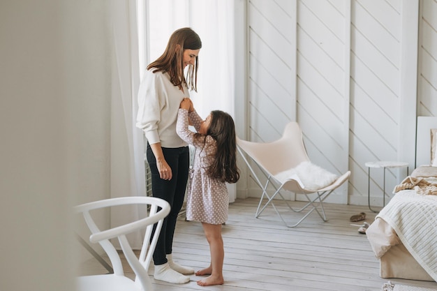 Photo cute long hair little girl helps dress her mother at the bright bed room