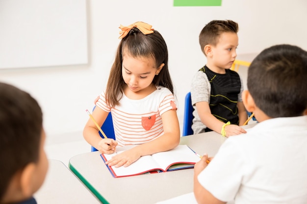 Photo cute looking hispanic preschool girl doing a writing assigment during class at school