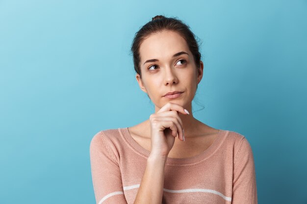 Cute lovely pensive young girl standing isolated over blue wall, thinking