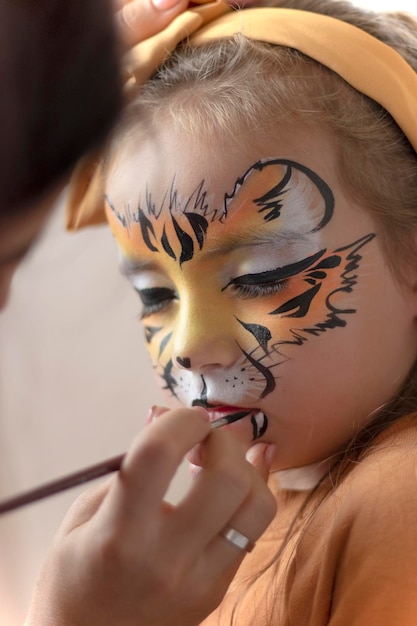 Foto piccola ragazza tigre con il trucco carino che si dipinge la faccia all'aperto