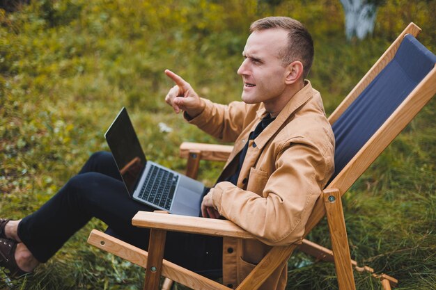 Cute man in a shirt sitting in a chair outdoors in the garden and working on a laptop remote work female freelancer