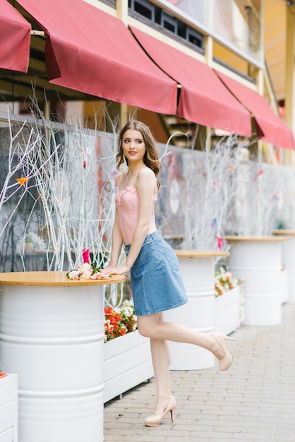 A cute model of a young beautiful woman in summer clothes stands near a white metal barrel 