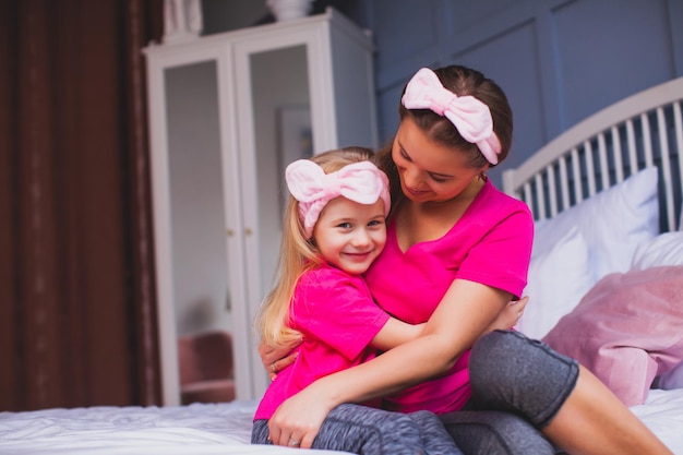 Cute mom and her little daughter are hugging in bed and cuddling after waking up