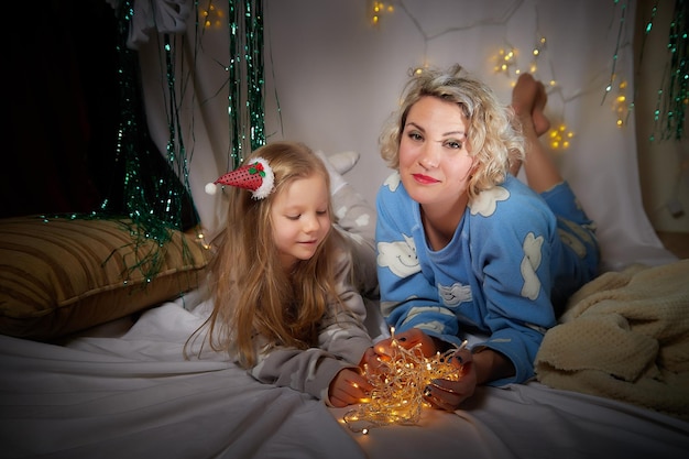 Cute mother and daughter lie on soft blanket and having fun in room with Christmas garlands