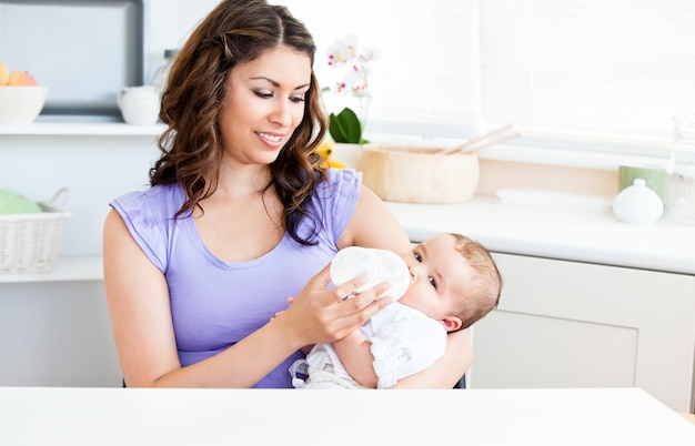 Cute mother feeding her baby siiting in the kitchen 