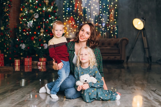 Cute mother with daughter and son posing at the Christmas tree