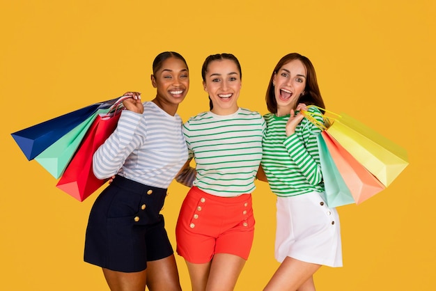 Cute multiracial ladies enjoying shopping together yellow background