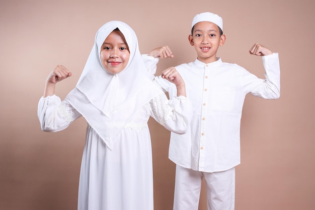 Cute muslim little kids boy and girl showing strong hands while looking at camera with happy express