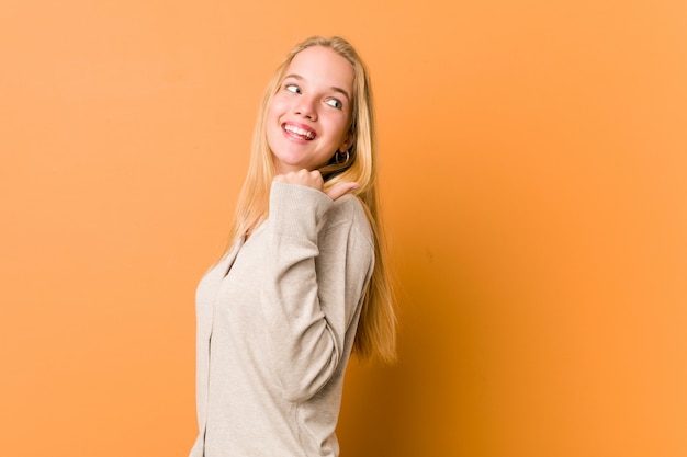 Cute and natural teenager woman points with thumb finger away, laughing and carefree.