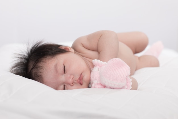 Cute newborn asian girl sleeping on the bed with no clothes. Sweet rose background.