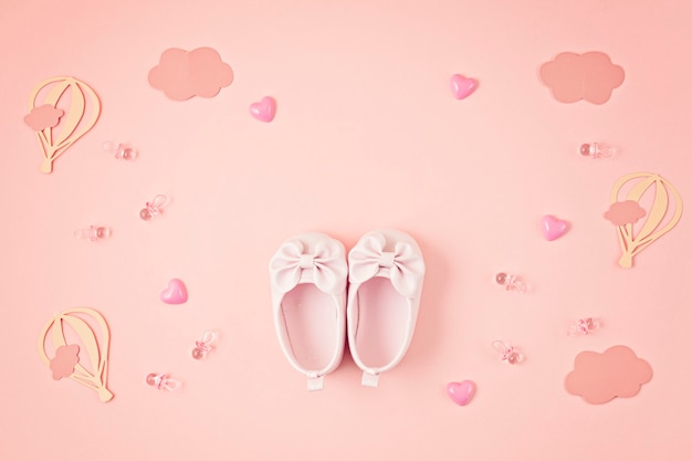 Cute newborn baby girl shoes with festive decoration over pink wall. 