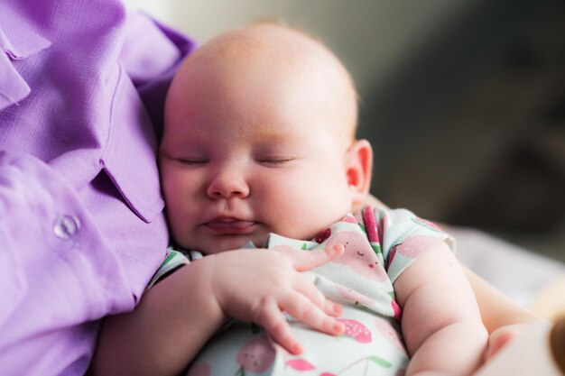 Cute newborn baby girl sleeping in her mothers arms closeup