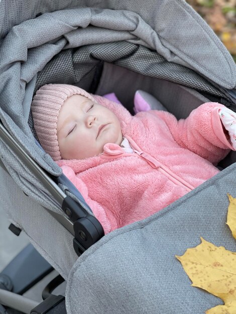 새로 태어난 귀여운 아기 소녀가 가을 공원에서 유니폼을 입고 잠을 자고 있습니다.