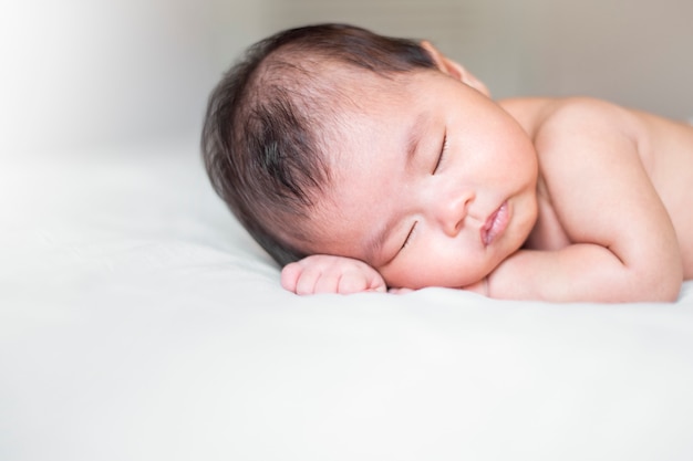 Cute newborn baby is sleeping on white bed 