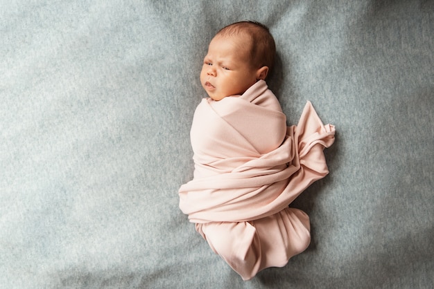 Cute newborn baby lies swaddled in pink blanket