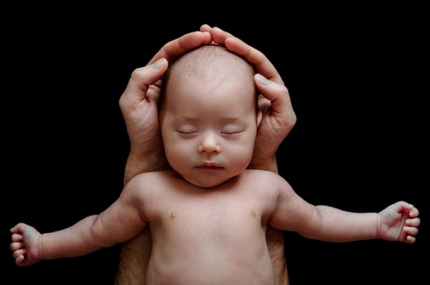 Cute newborn baby lying in the father's hands on black background