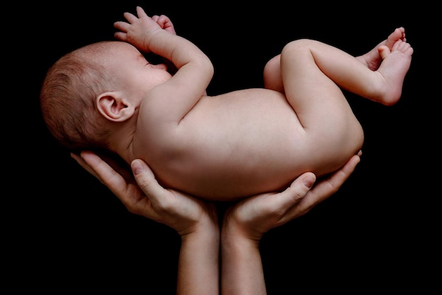 Foto neonato sveglio che giace nelle mani della madre su sfondo nero