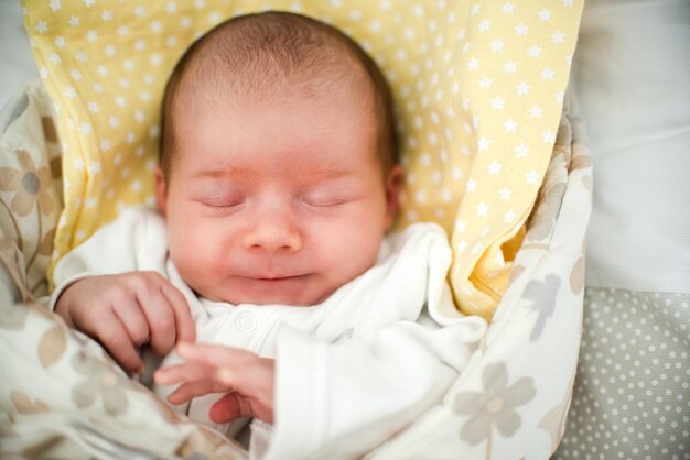 Cute newborn baby sleeping in swaddle wrap with smile on her face