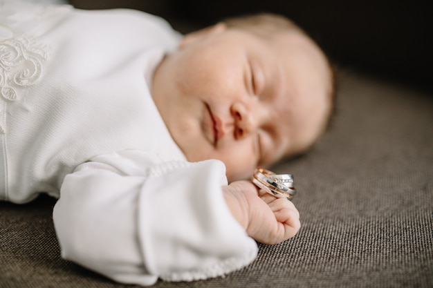 かわいい生まれたばかりの赤ちゃんがベッドで寝て、金の指輪を保持