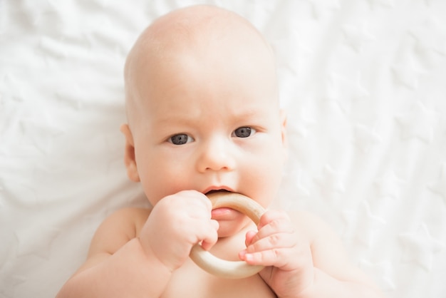 Cute newborn baby takes a wooden toy in his mouth
