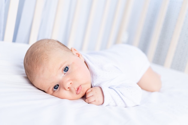 Cute newborn baby on tummy in crib on cotton bed at home, healthy sleep concept.