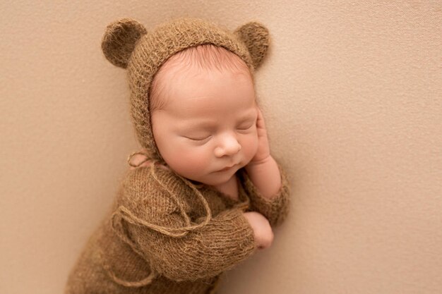 A cute newborn boy in the first days of life sleeps in a brown bear overalls a hat with bear ears Professional studio macro photo on a brown background High quality photo