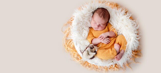 Милый новорожденный в желтом вязаном костюме, лежащий в колыбели для яиц