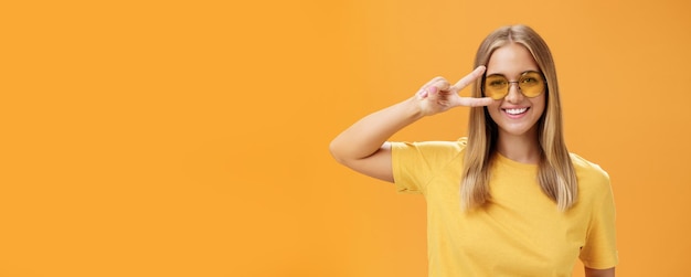 Foto carina, ottimista e amichevole giovane donna caucasica con i capelli biondi, maglietta gialla e occhiali da sole.