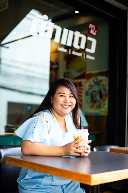 コーヒーカフェでかわいい太りすぎの女性、プラスチック製のコップコーヒーとカフェで幸せなアジアの女性