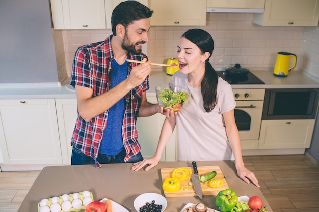 Cute picture of man standing at table and holding bowl with salad.