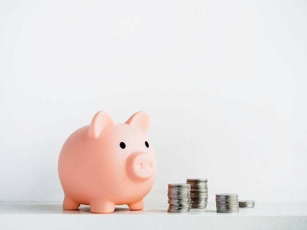 Photo cute piggy bank with piles of coins isolated on white surface