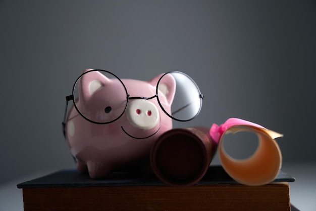 Photo cute piggy bank with round eyeglasses on stack of books and scroll certificate