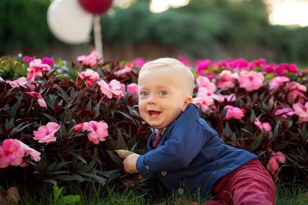 かわいい遊び心のある笑顔の金髪。風船で遊ぶ緑の芝生の上に座っている1歳の男の子。