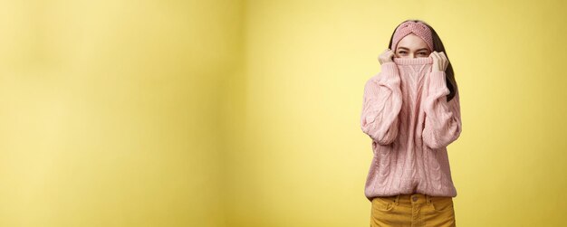 Photo cute playful young girl hiding in sweater peeking and squinting flirty over top of cloth pulling