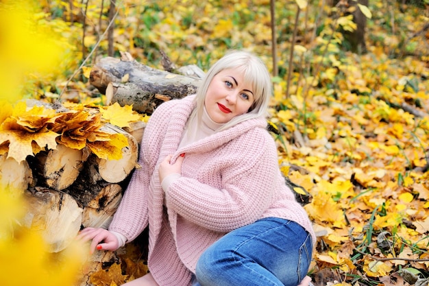 Cute plump middleaged blonde posing on a sunny autumn day in the woods in a knitted jumper