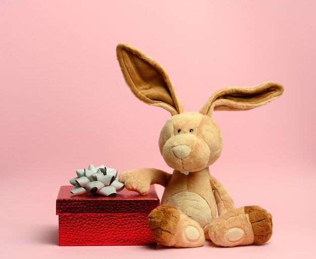 Cute plush rabbit holding a red gift box, pink wall