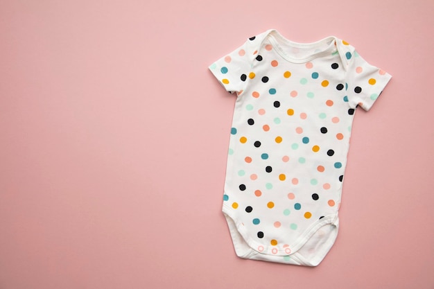 Cute polka dot baby body suit layout on a pastel pink background