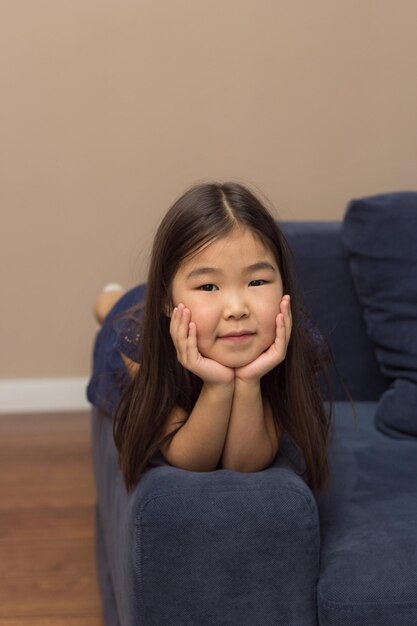 Cute portrait of little smiling girl pretty adorable asian child lying on couch looking at camera