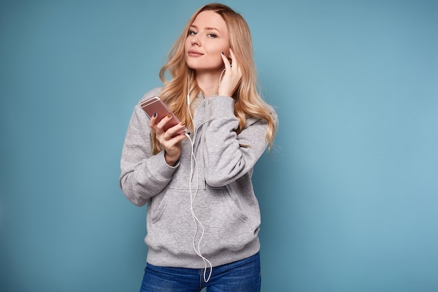 Cute positive blonde woman in hoodie listening music